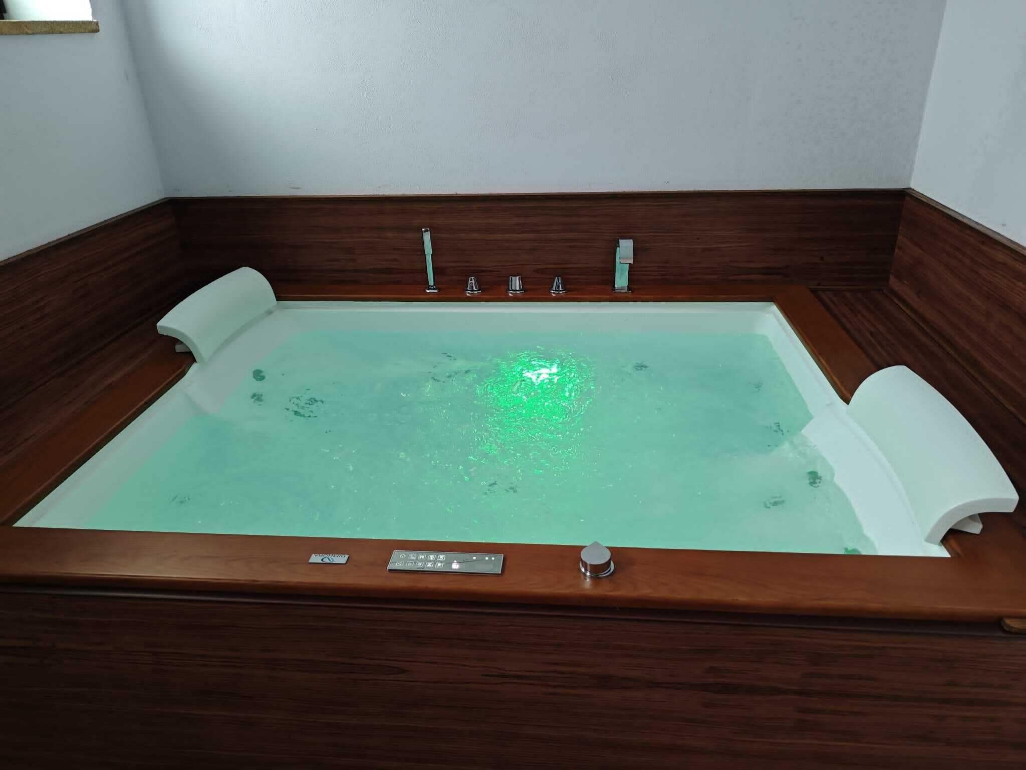 Un bain à remous rectangulaire doté d’une structure en bois et d’un panneau de commande situé en bas.