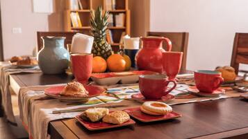 A dining table set with plates, cups, and a pitcher, surrounded by bookshelves and a pineapple.