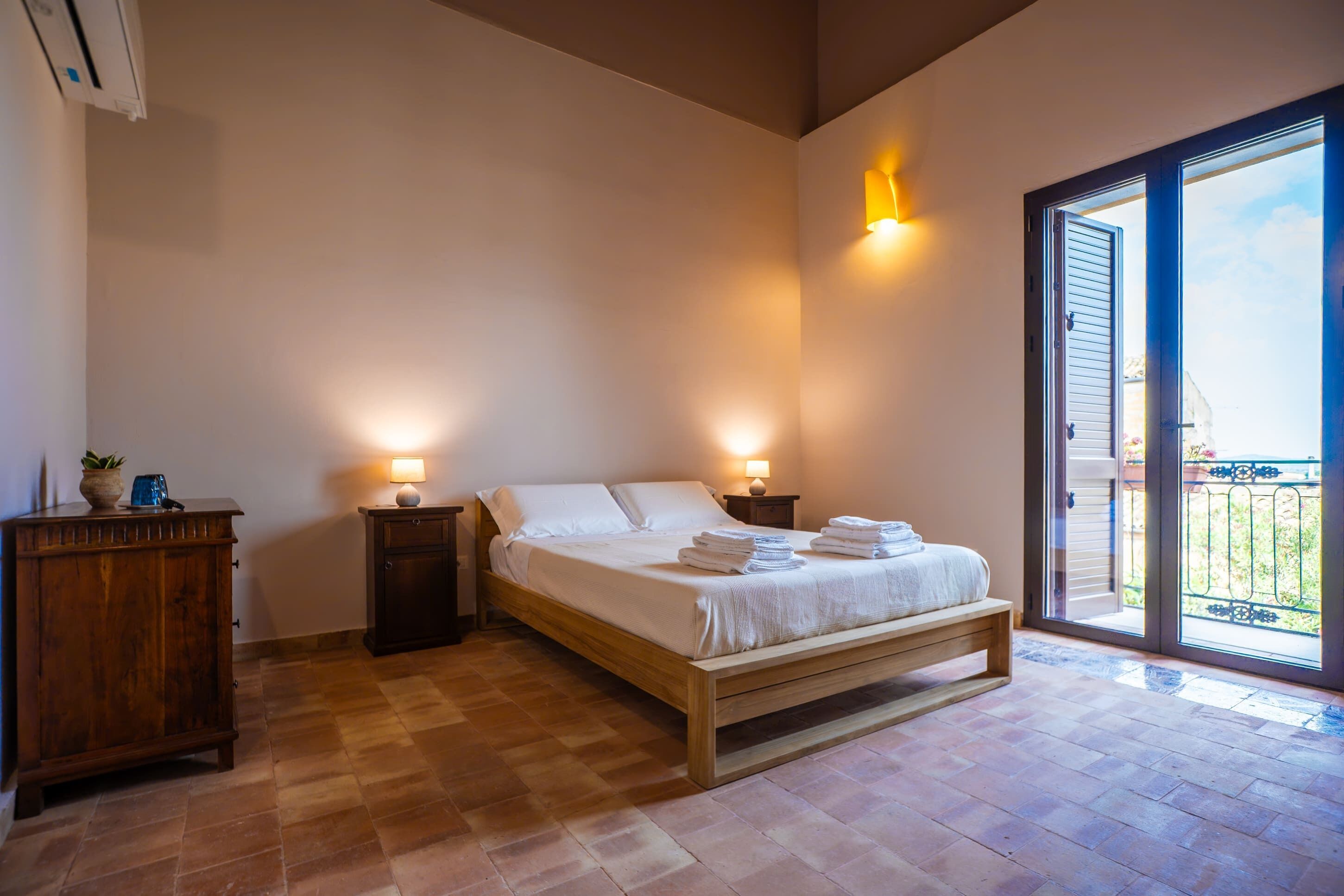 A bedroom with a wooden bed, two bedside tables, a nightstand, a dresser, and a sliding glass door to a balcony.