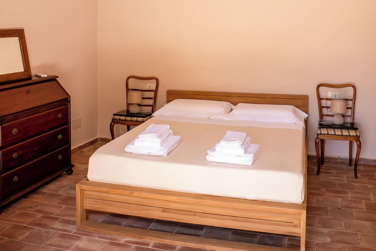 Ein Schlafzimmer mit einem hölzernen Bett, zwei Stühlen, einer Kommode und einer Decke mit floralen und runden Mustern.