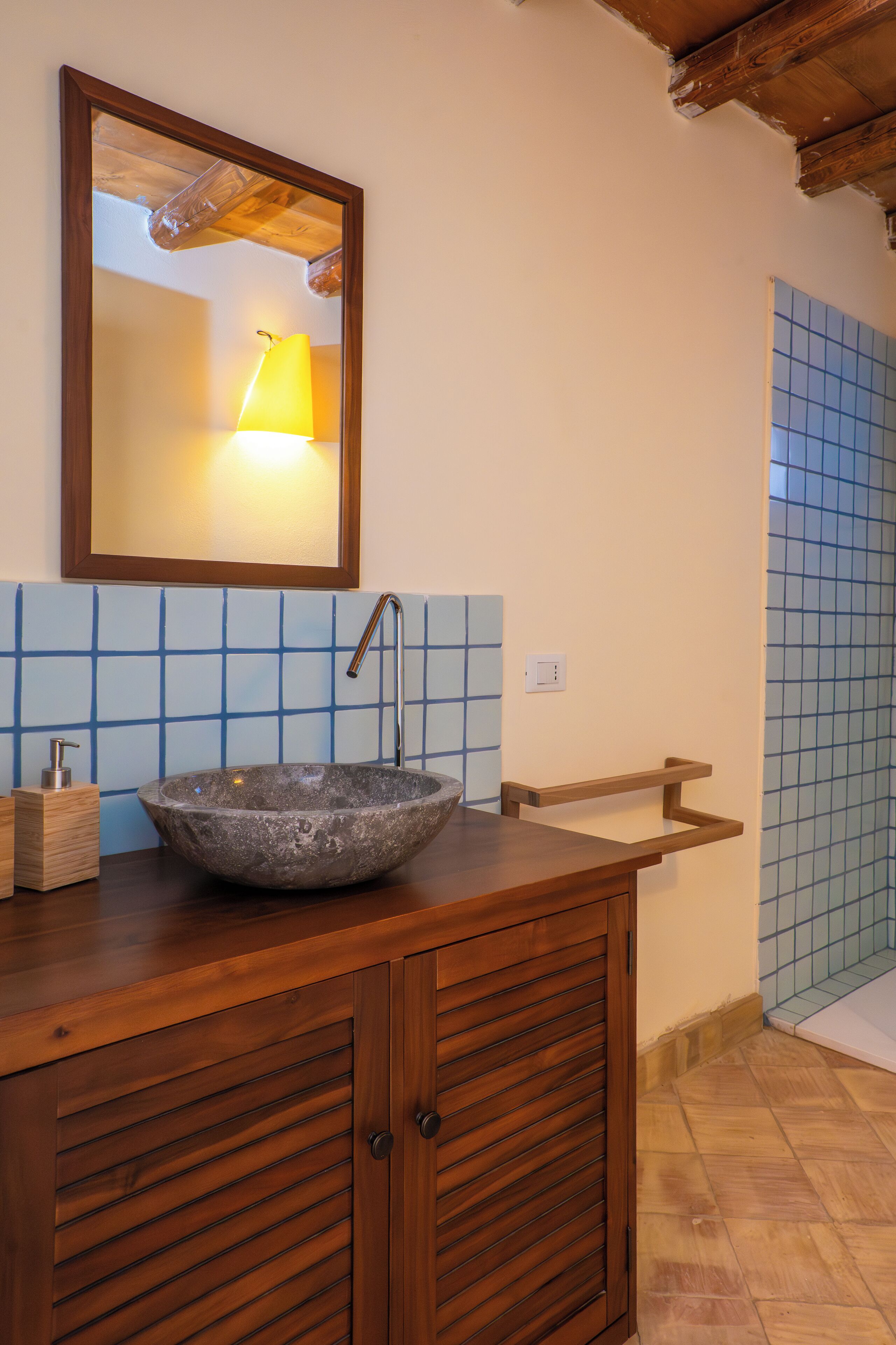 Un baño con tocador de madera, lavamanos de piedra, espejo y paredes cubiertas de azulejos azules.