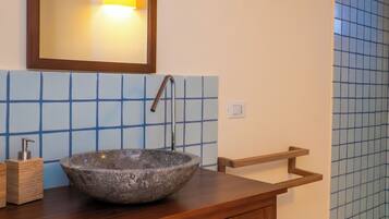 Un baño con tocador de madera, lavamanos de piedra, espejo y paredes cubiertas de azulejos azules.