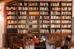 A room with a large wooden bookshelf filled with books, a dining table with chairs, and a kitchen area with wooden cabinets.