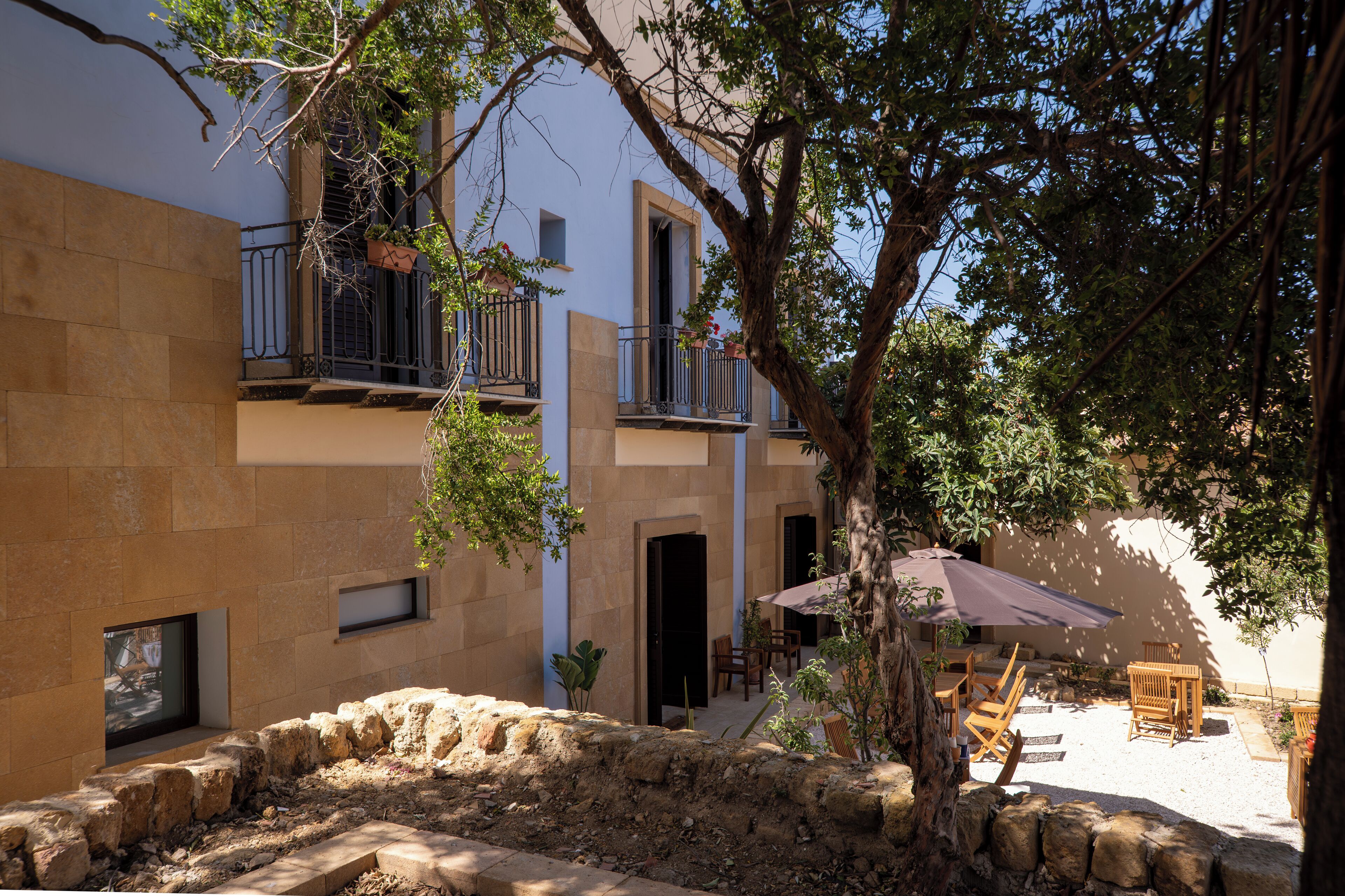 Un patio con muros de piedra, un árbol y mobiliario exterior.