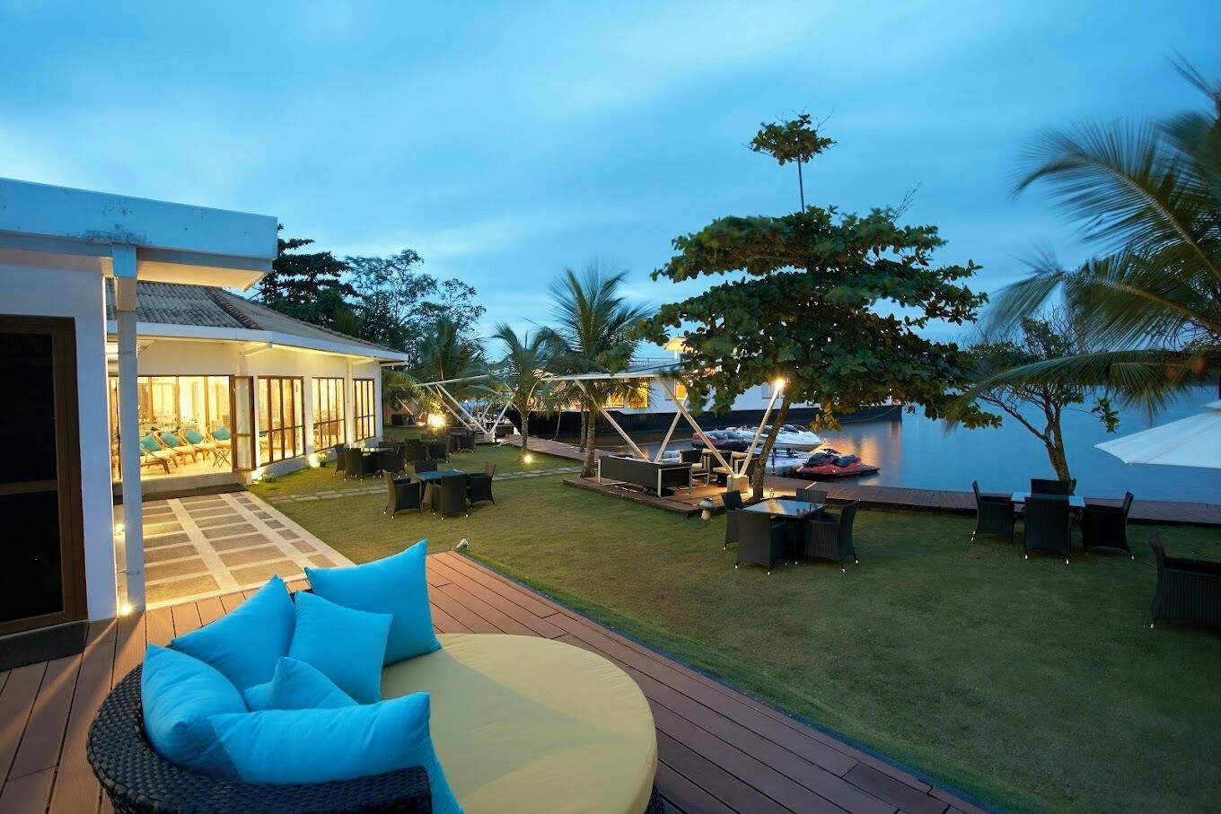 Un patio exterior bien iluminado con mobiliario, una piscina y vistas al agua.