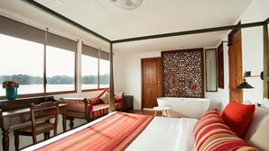 A bedroom with a large bed, a desk, a chair, a window, a bathtub, and a decorative wall panel. - Houseboats By DAE Colombo (Piliyandala)
