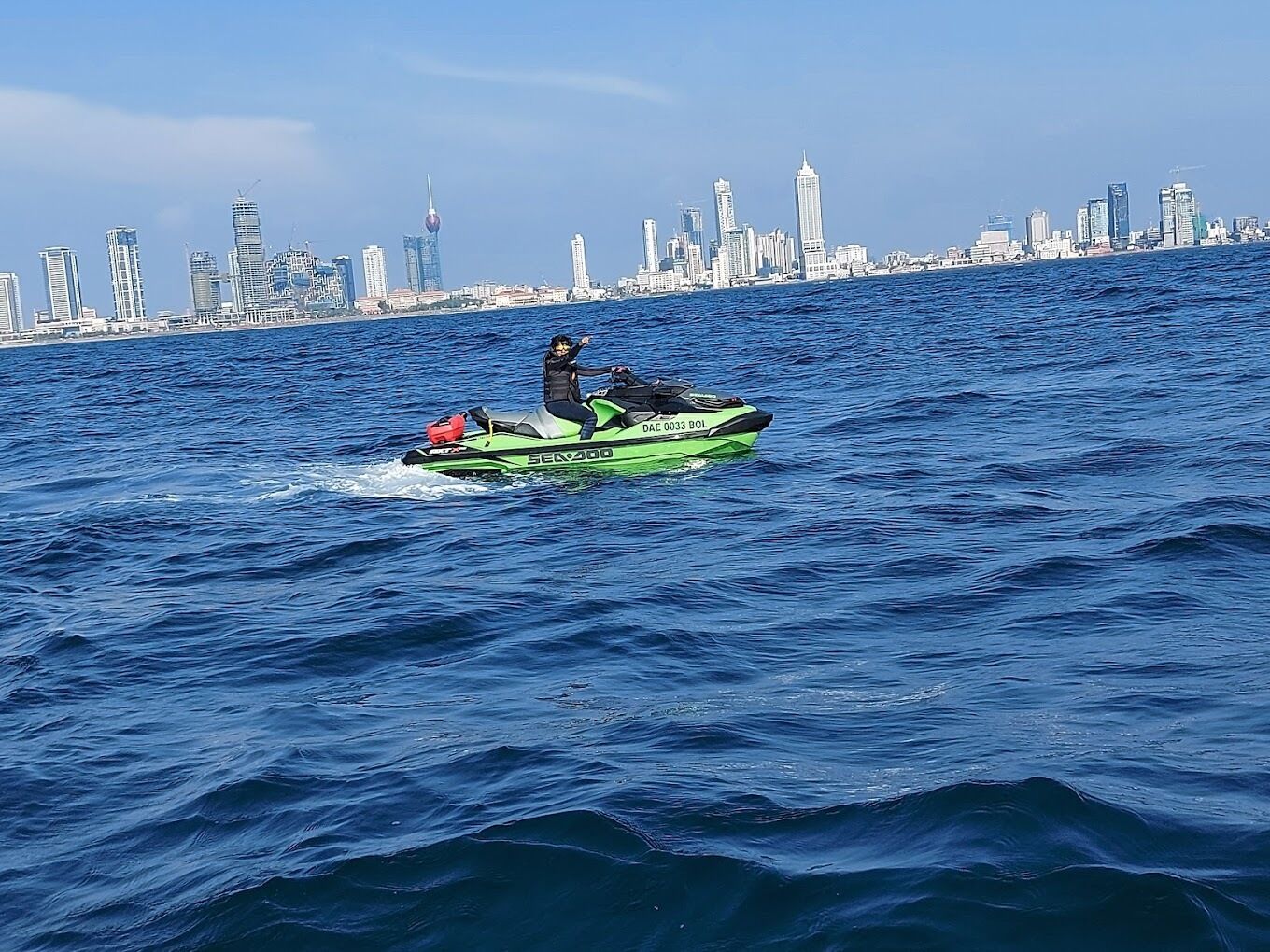 A person riding a green jet ski on a body of water with a city skyline in the background.