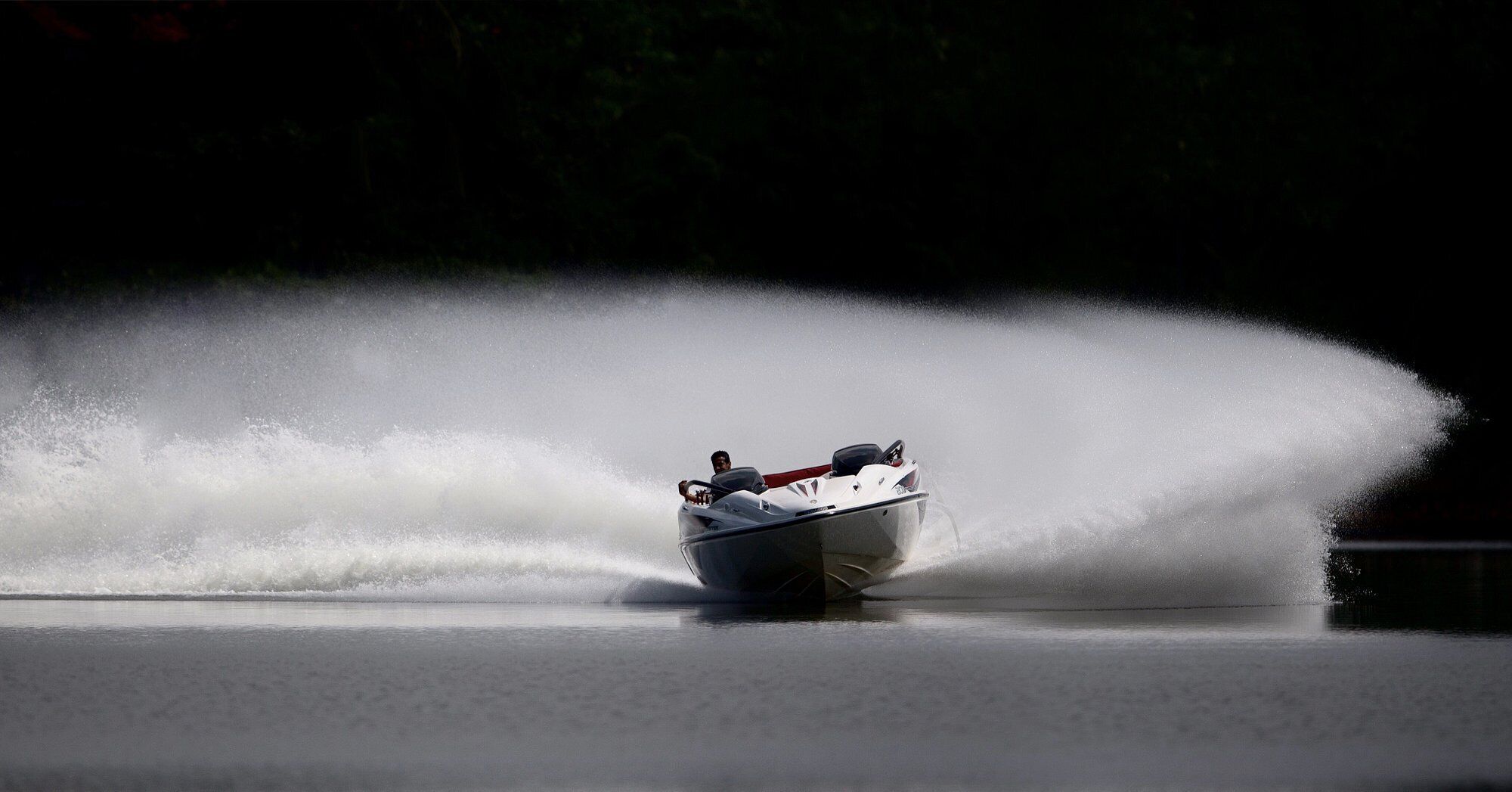 A speedboat creating a large water spray on a calm body of water.
