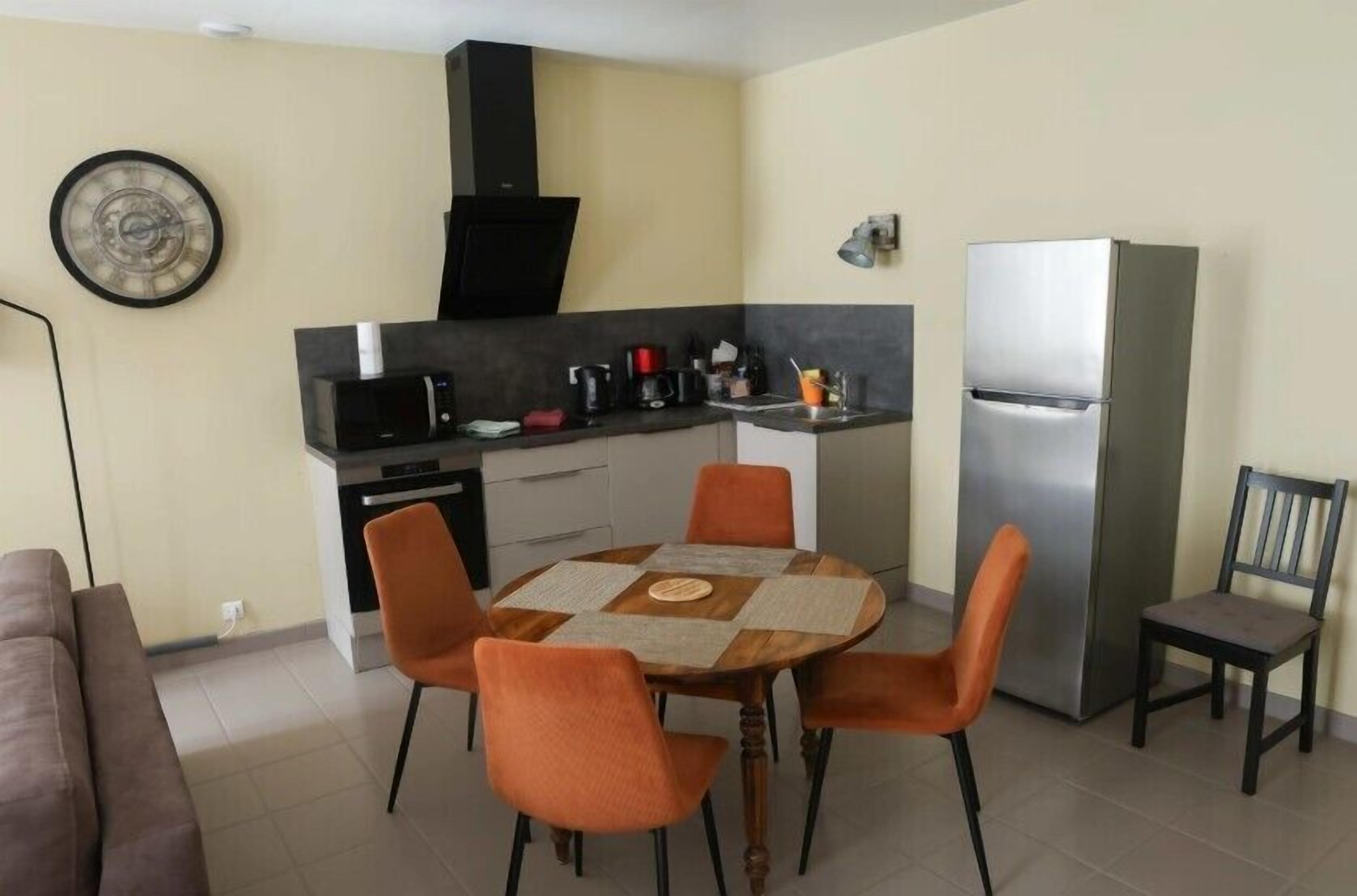 A compact kitchen with a dining table, chairs, a refrigerator, and a microwave.