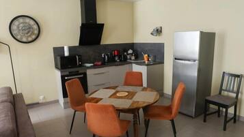 A compact kitchen with a dining table, chairs, a refrigerator, and a microwave.