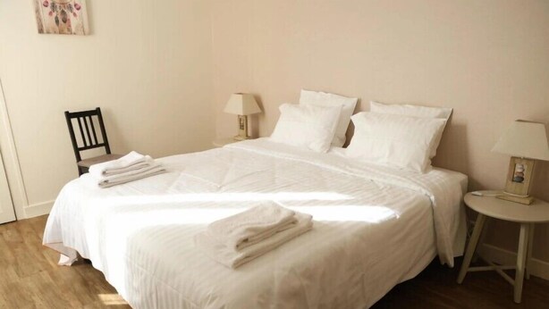 A neatly made bed with white linens and towels, a small wooden chair, and two bedside tables with lamps. - Chablis Appart (Chablis)