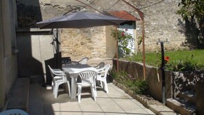 An outdoor patio with a table and chairs, a large umbrella, and a stone wall. - Chablis Appart (Chablis)