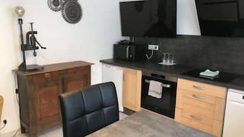 A compact kitchen with a dining table, a black chair, a wooden cabinet, a black countertop, a black stove, and a black oven.
