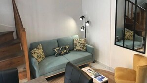 A living room with a green sofa, a black armchair, a coffee table with magazines, and a staircase. - Chablis Appart (Chablis)