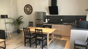 A modern kitchen with a wooden table and chairs, a black range hood, and a clock on the wall. - Chablis Appart (Chablis)