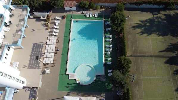 Vue aérienne d’un hôtel doté d’une piscine, de chaises longues et d’un court de tennis.