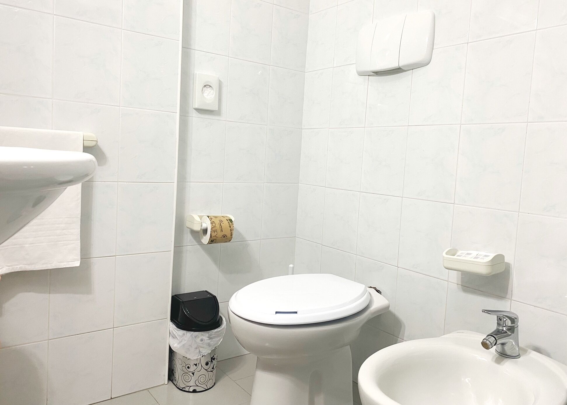Et badeværelse med toilet, bidet, vask og skraldespand.