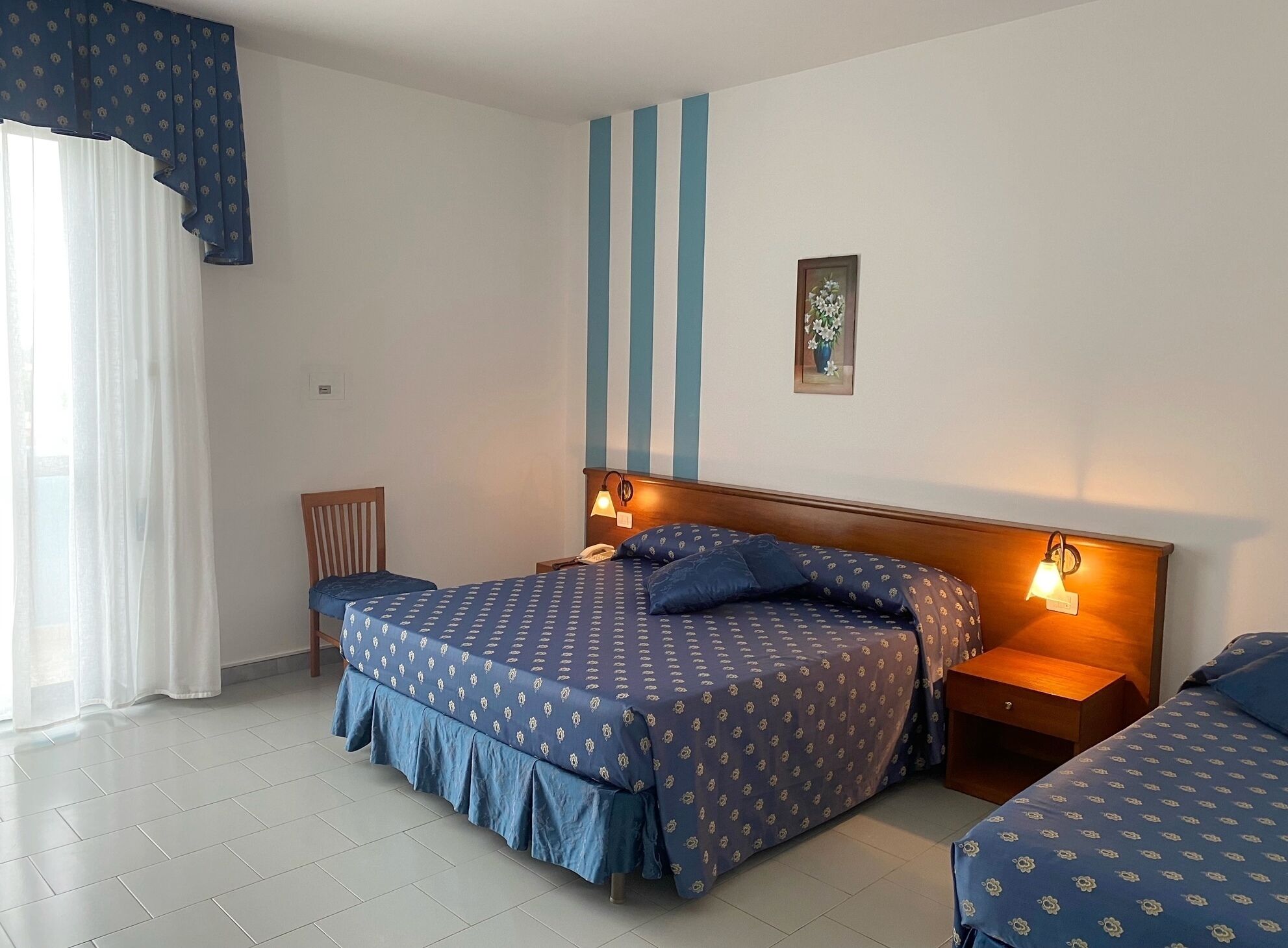 Un dormitorio con cama, mesitas de noche, una silla y una ventana con cortinas.