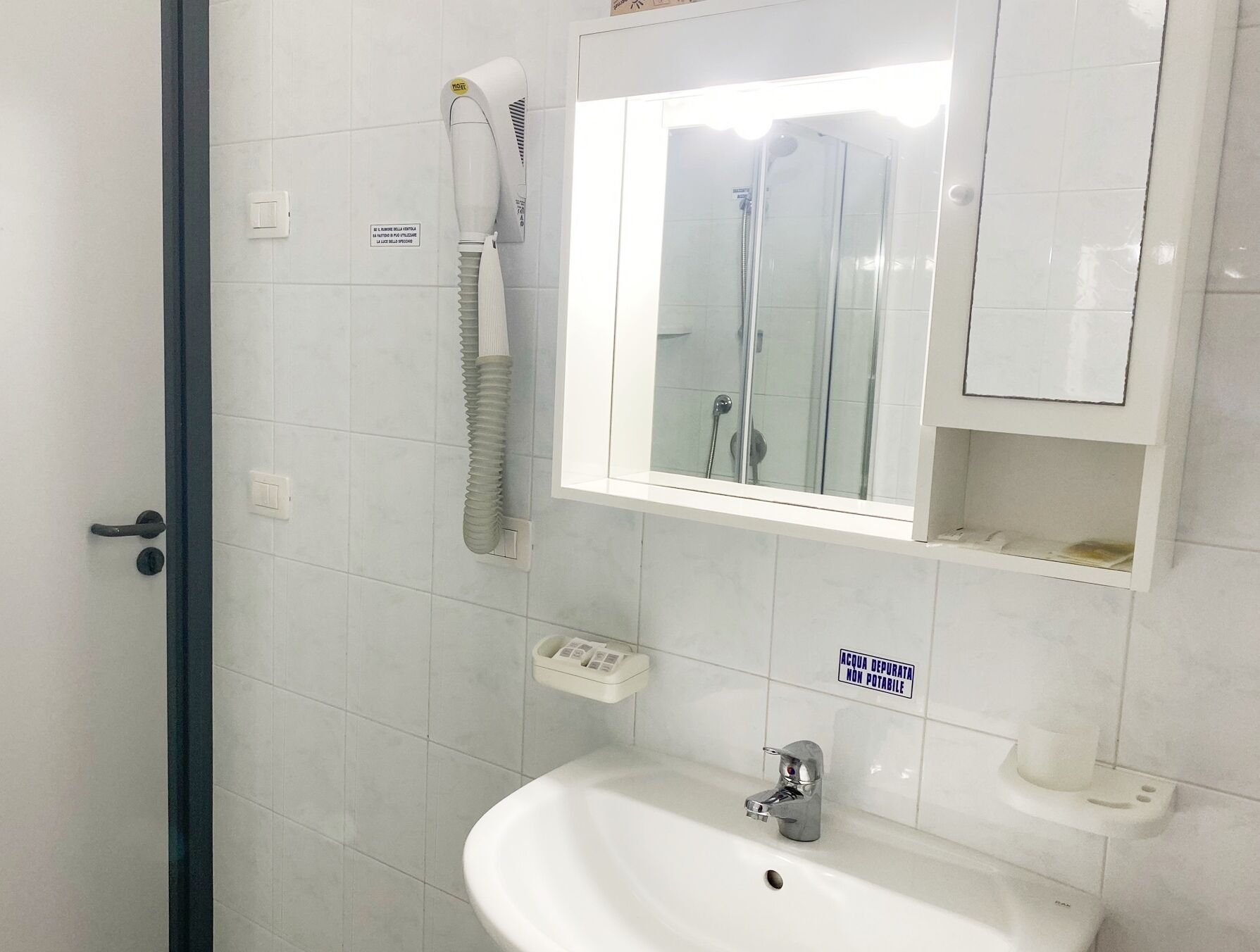 A bathroom with a white sink, a mirror, a glass-enclosed shower, and a telephone mounted on the wall.