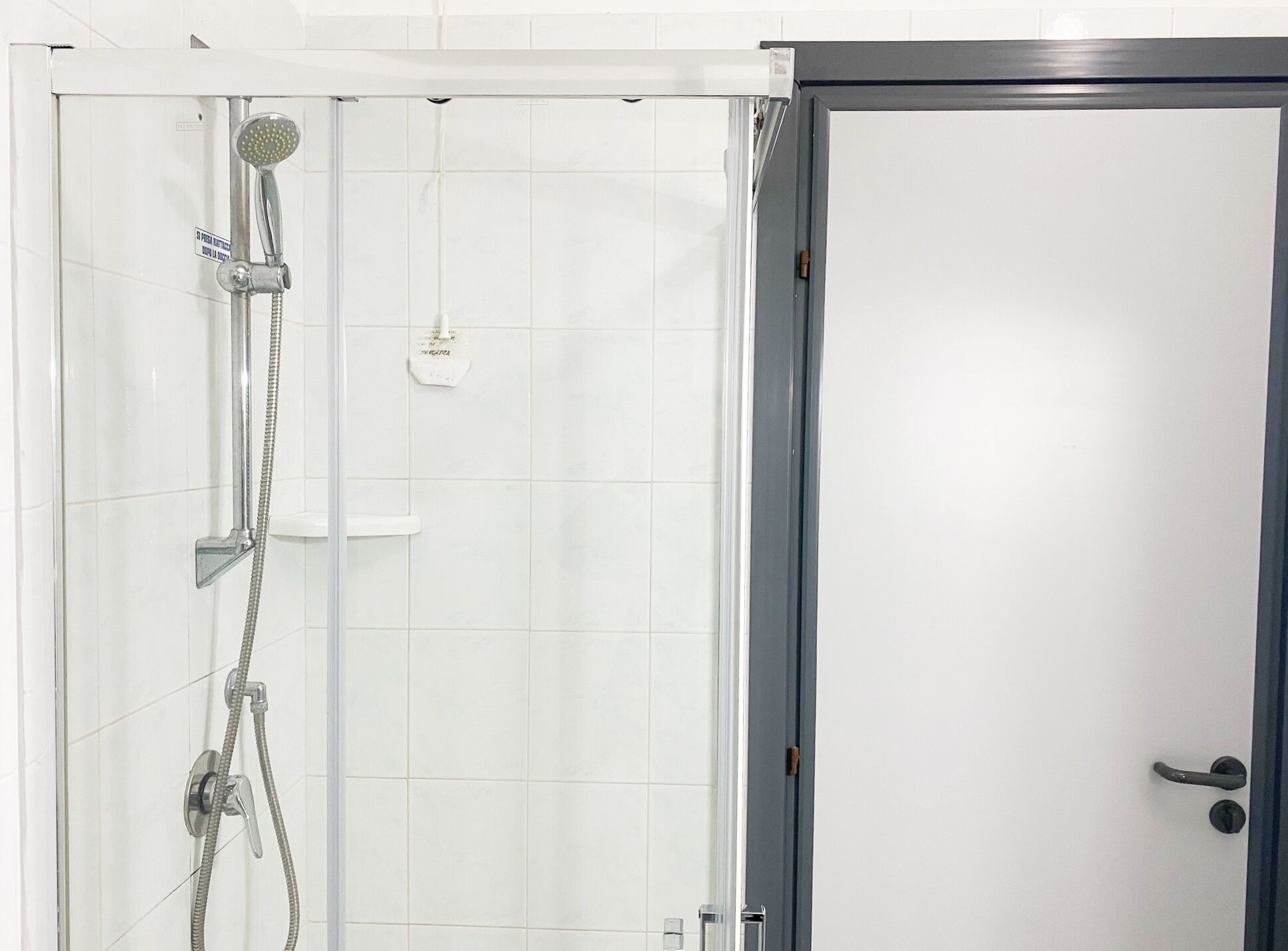 Une salle de bain moderne avec une douche à parois de verre, un mur recouvert de carreaux blancs et une porte dotée d’une poignée noire.