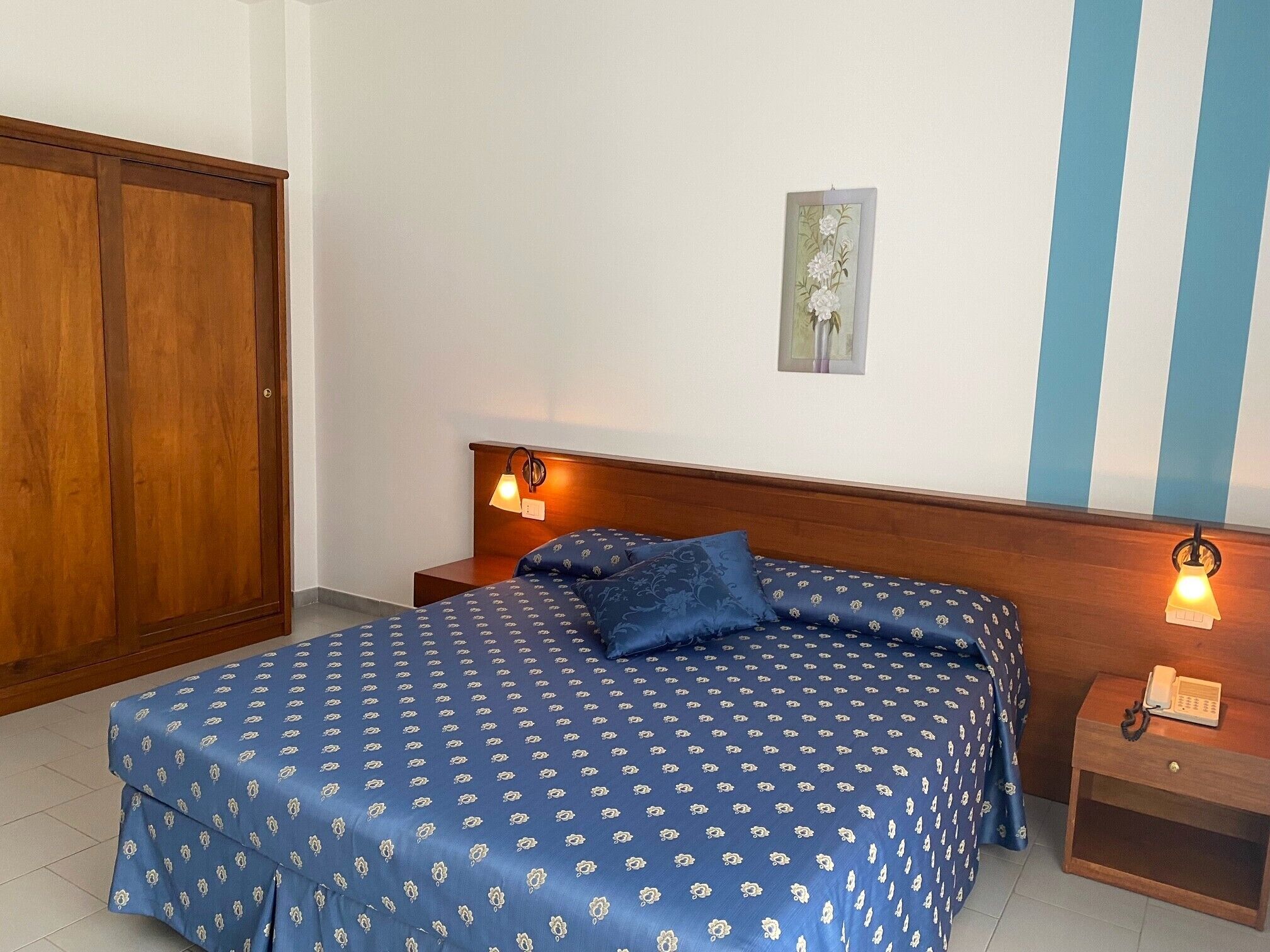 A bedroom with a large bed, two bedside tables, a wooden wardrobe, and a wall-mounted light fixture.