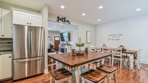 A modern kitchen with a stainless steel refrigerator, wooden dining table, and white cabinetry. - The Montreat House (Black Mountain)