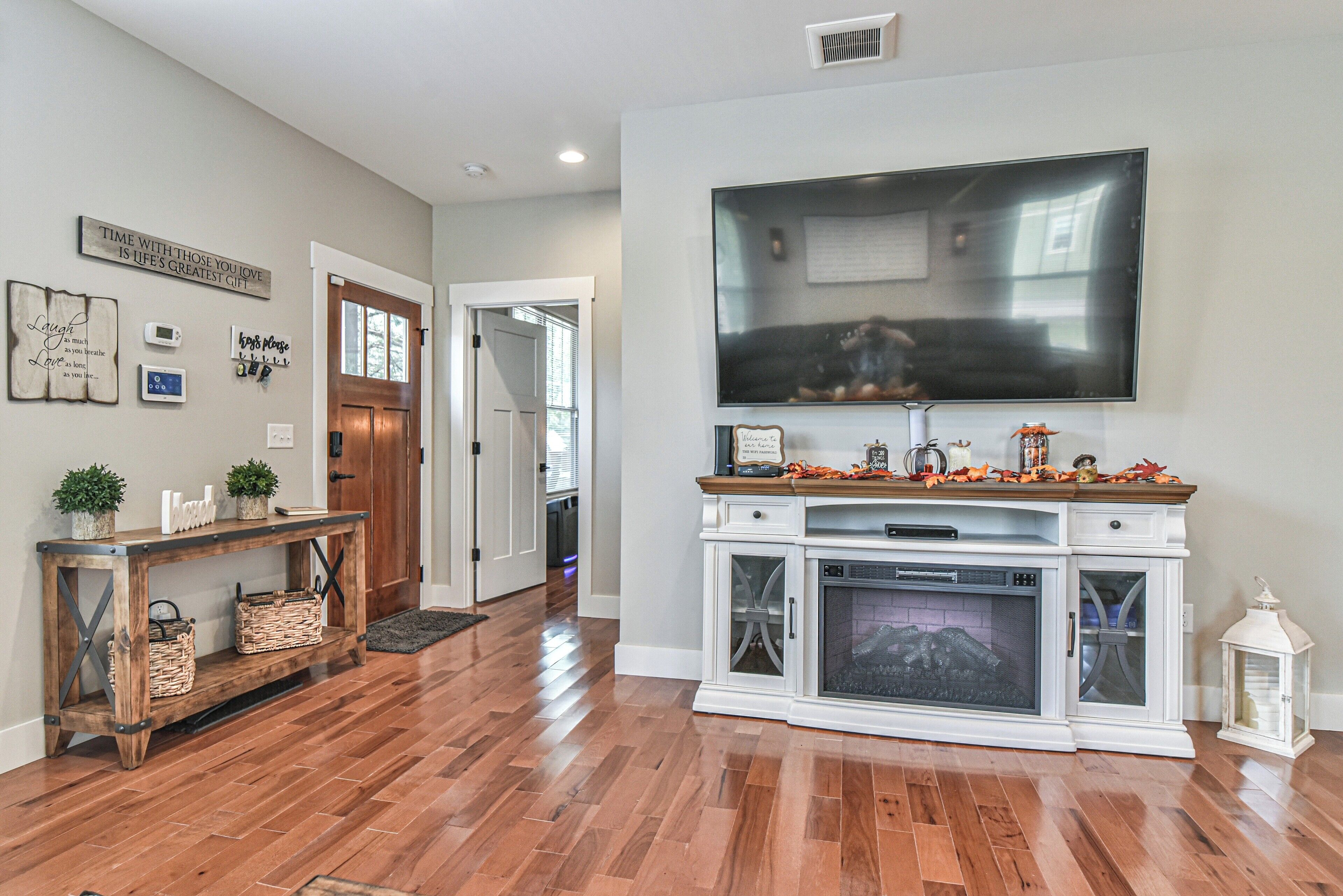 A living room with hardwood flooring, a fireplace, a large flat-screen TV, and a console table with decorative items.