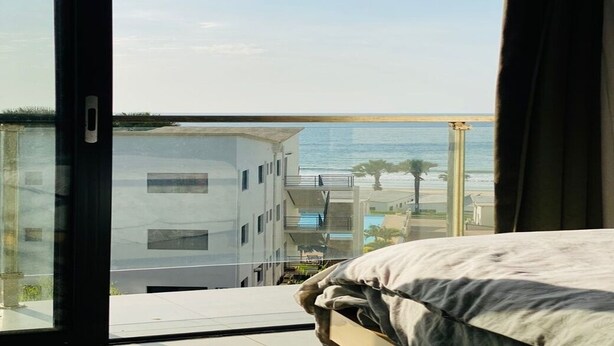 Ett hotellrum med ett stort fönster med utsikt över en strand och en modern byggnad.