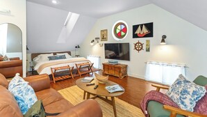 Ruime loft slaapkamer met een groot bed, een televisie en een gezellige zithoek met een salontafel en stoelen.