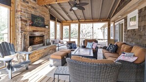 A cozy outdoor seating area with wicker furniture, a stone fireplace, and large windows.
