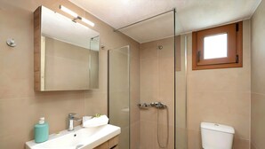 Een moderne badkamer met een glazen douchecabine, een wit wastafelmeubel met een houten blad en een toilet.