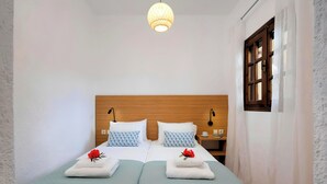 Een knus kamertje met twee bedden, een houten hoofdbord, een nachtkastje met een lamp en een raam met gordijnen.