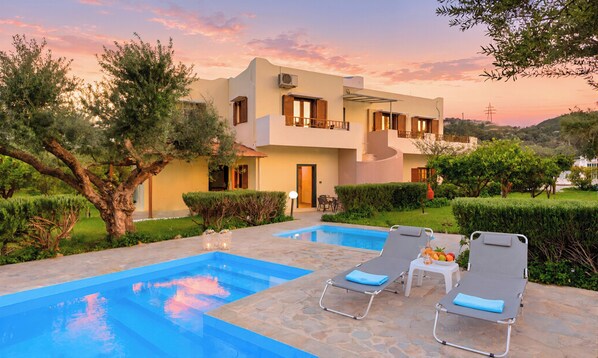 A two-story building with a swimming pool, lounge chairs, and a well-maintained garden.