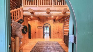 Interior de uma cabana de madeira com escada de madeira, um tapete grande e uma coroa de Natal.