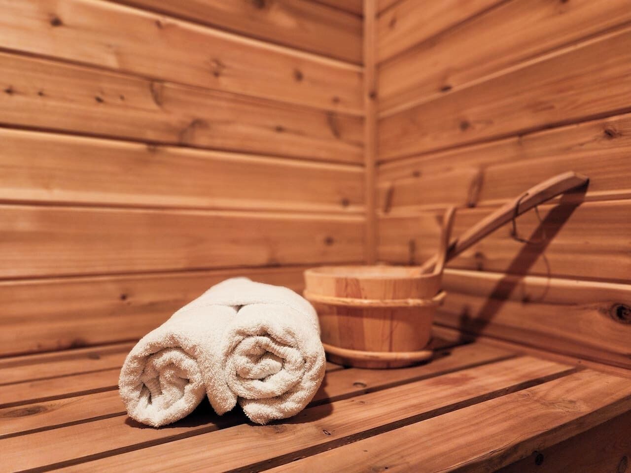 A wooden sauna with a bench, a towel, and a wooden bucket.