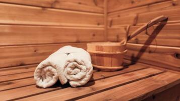 A wooden sauna with a bench, a towel, and a wooden bucket.