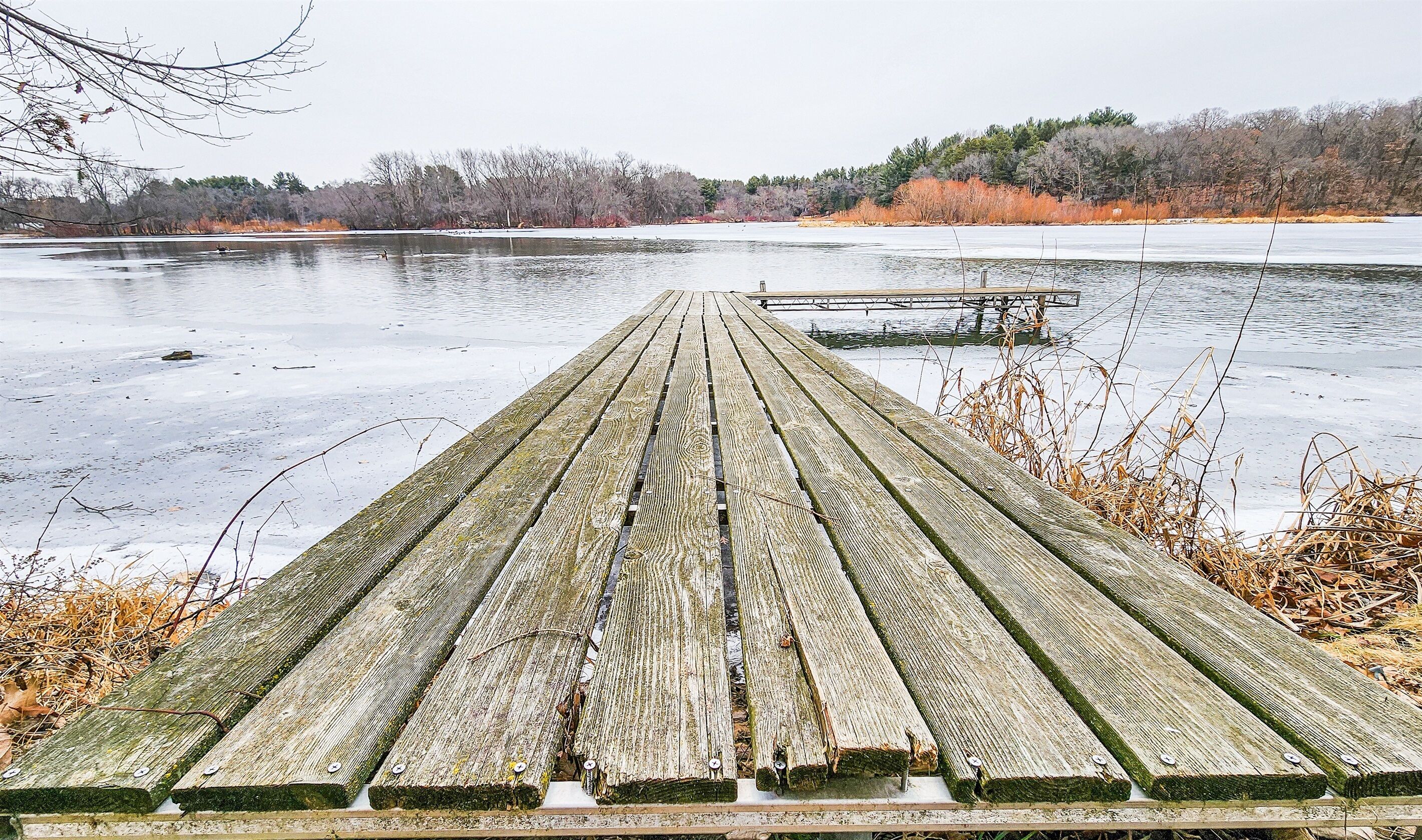 Une jetée en bois s’étendant sur un lac gelé, avec un banc à son extrémité.
