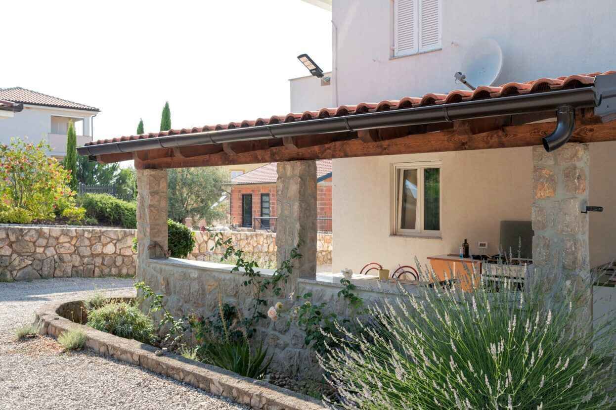 A covered outdoor area with stone pillars, a gravel path, and various plants.