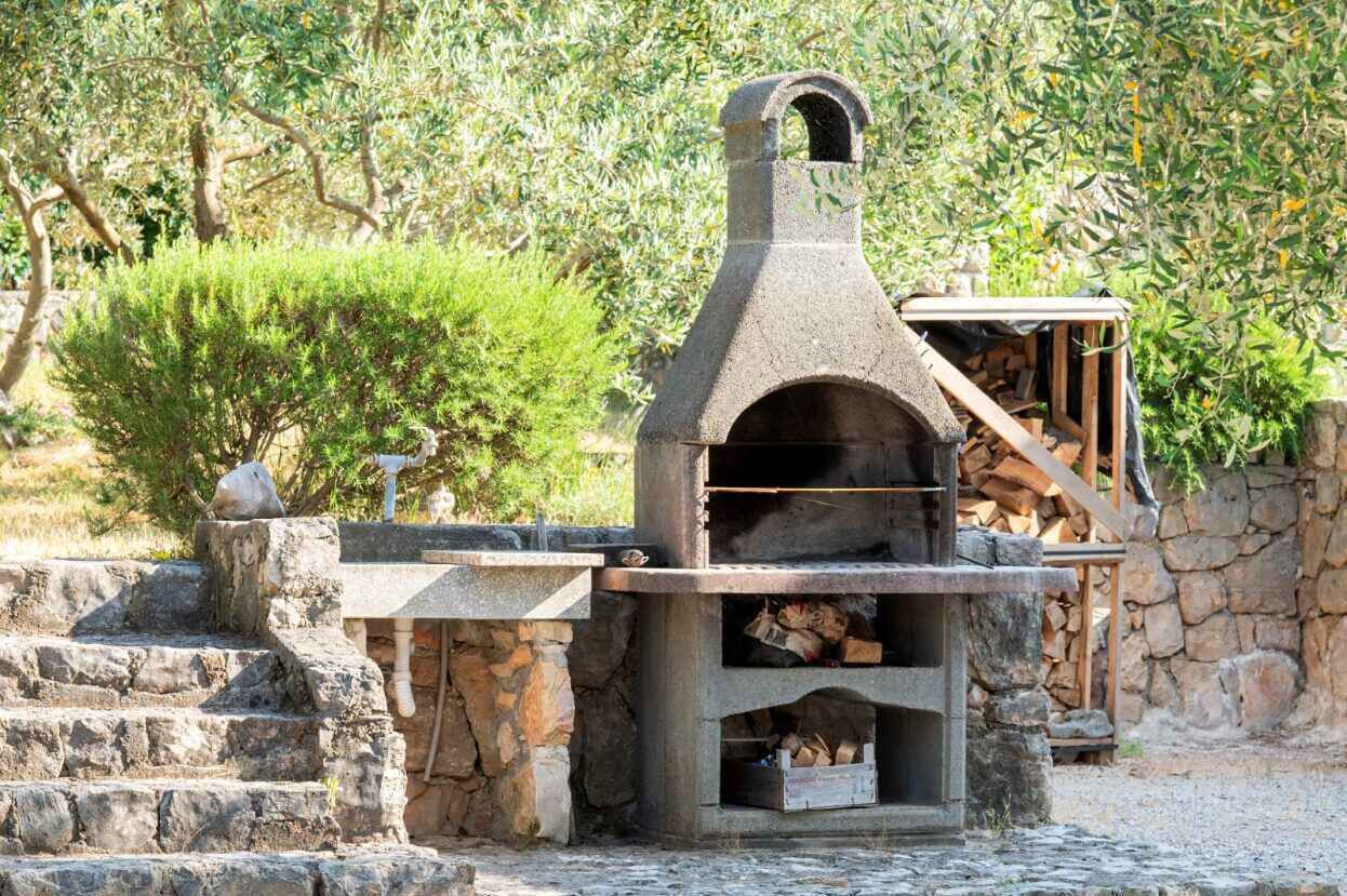 A stone-built outdoor oven with a chimney, surrounded by stone steps and a small wooden structure.