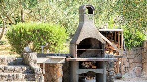 Un horno de piedra al aire libre con chimenea, rodeado de escalones de piedra y una pequeña construcción de madera.