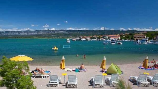 Una playa con tumbonas, sombrillas y una vista despejada de barcos en el agua.