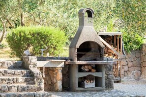 A stone-built outdoor oven with a chimney, surrounded by stone steps and a small wooden structure.