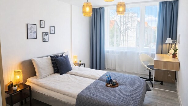 A modern hotel room with a bed, bedside table, desk, chair, and large windows with curtains. - Family - by Kairos Apartments (Gliwice)