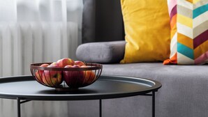 A bowl of apples on a round table in a living room with a gray sofa and colorful pillows. - Family - by Kairos Apartments (Gliwice)
