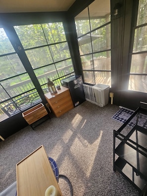 A room with large windows, a radiator, a wooden dresser, a small table, and a chair.