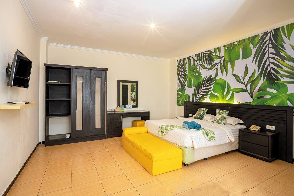 Ein Schlafzimmer mit Bett, Nachttisch, Schreibtisch, Kleiderschrank und Fernseher.