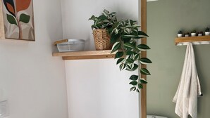 Un baño con una mesa de madera, una planta colgante, un estante con una cesta y un tazón, un perchero para toallas y un inodoro.