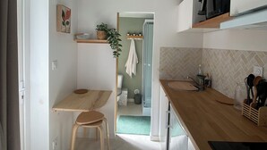 Cocina compacta con encimera de madera, un taburete pequeño, un ventilador de techo y vistas al baño contiguo.