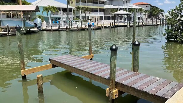 A wooden dock extending into calm water with a marina in the background featuring multi-story buildings and docks. - Stay and Play by the Bay 
Boaters Delight. Waterfront ,Dockage and Heated Pool

 (Fort Myers Beach)