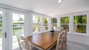 A spacious dining area with a wooden table and white chairs, large windows with tropical views, and a small sailboat model on the table. - Stay and Play by the Bay 
Boaters Delight. Waterfront ,Dockage and Heated Pool

 (Fort Myers Beach)